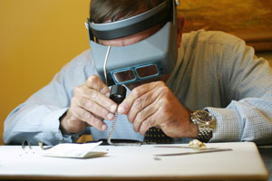 a jeweler, wearing a binocular headband magnifier, examines bracelet diamonds