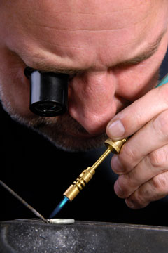 jeweler, wearing an eyepiece magnifier, using a soldering iron to repair a silver ring